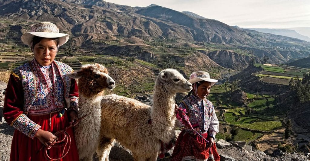 Dos jovencitas nativas de Chivay posando con sus llamas en vestimenta tradicional, de fondo el espectacular Valle del Colca.