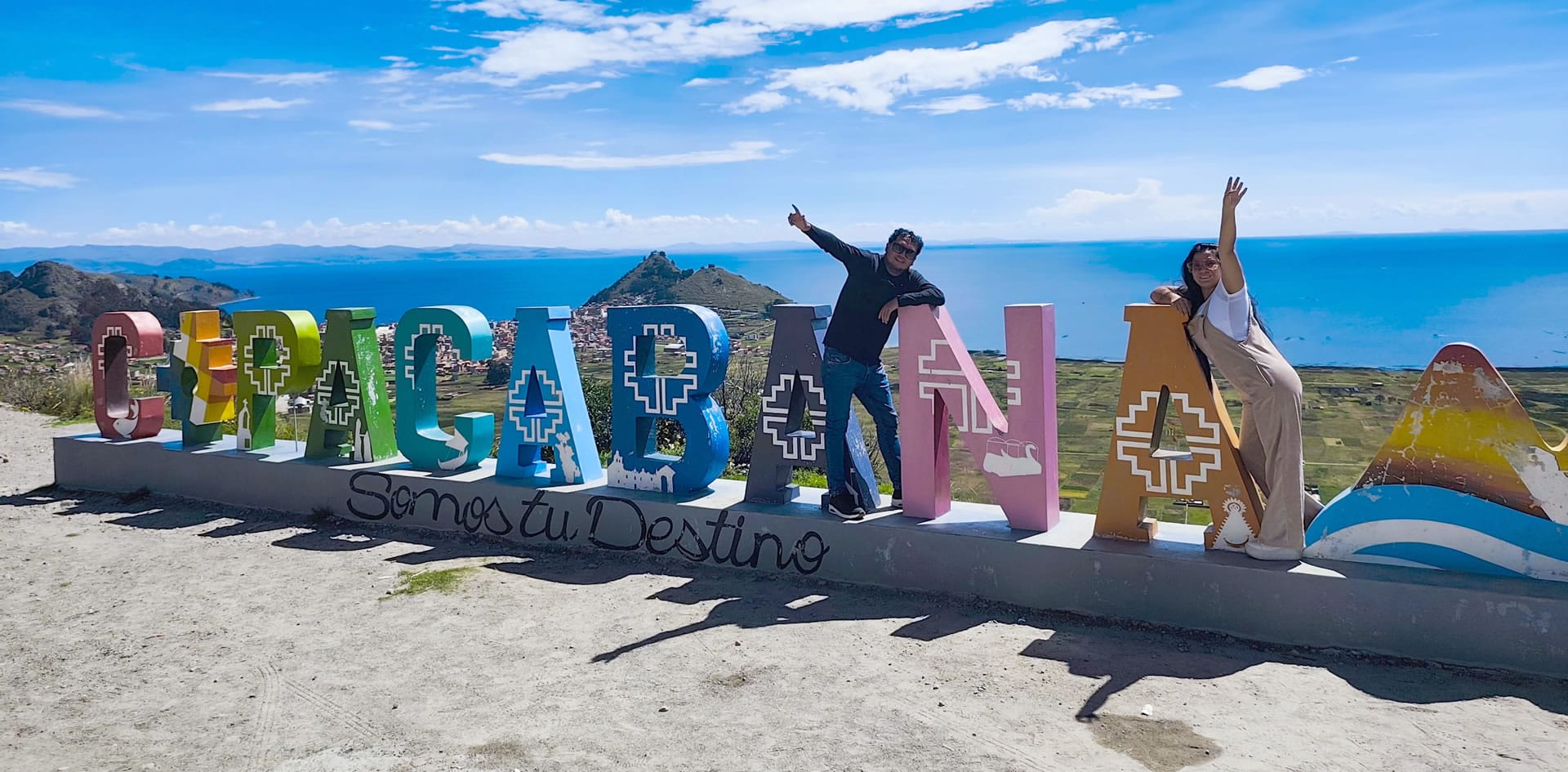 Pareja de viajeros posando junto al letrero corpóreo COPACABANA al llegar en el bus directo Puno - Copacabana.