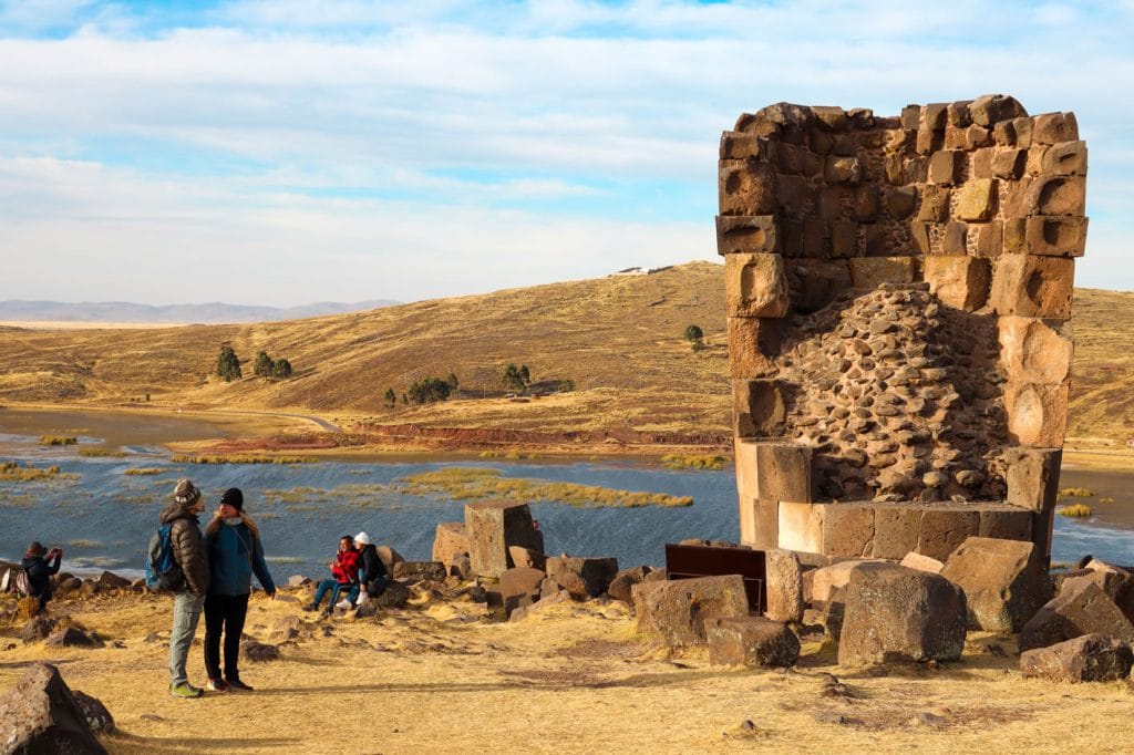 Chullpas funerarias en construcción de la cultura Ccolla en Sillustani, hacia la derecha algunos turistas contemplando y otros tomando fotografías.