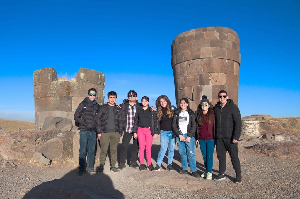 Chullpas funerarias uno completo y el otro en proceso de construcción en Sillustani, al frente un grupo de turistas posando muy sonrientes.