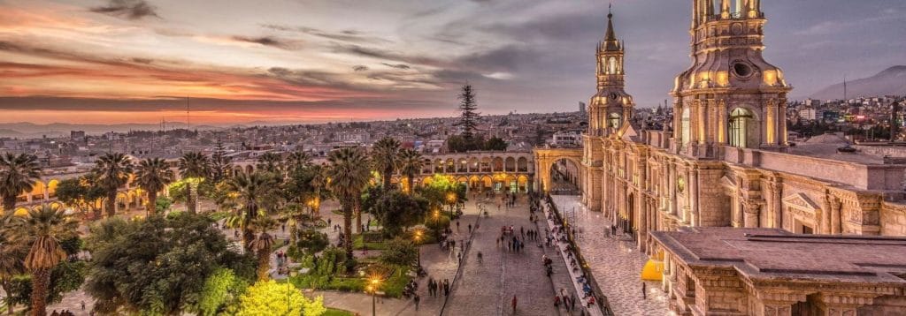 Vista lateral de la Plaza de Armas de Arequipa al atardecer, destacando la silueta de la Catedral de sillar contra el cielo anaranjado.
