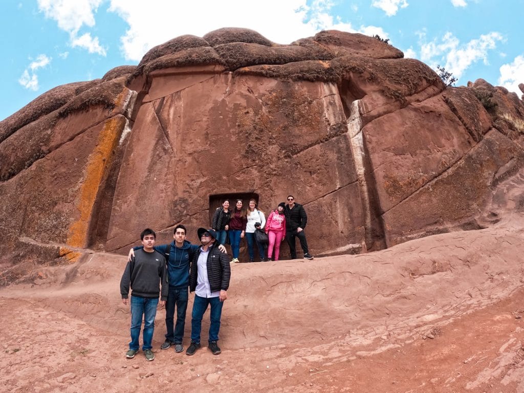 Grupos de turistas posando frente al Portal Dimensional de Aramu Muru, con vista completa de la gran roca tallada.