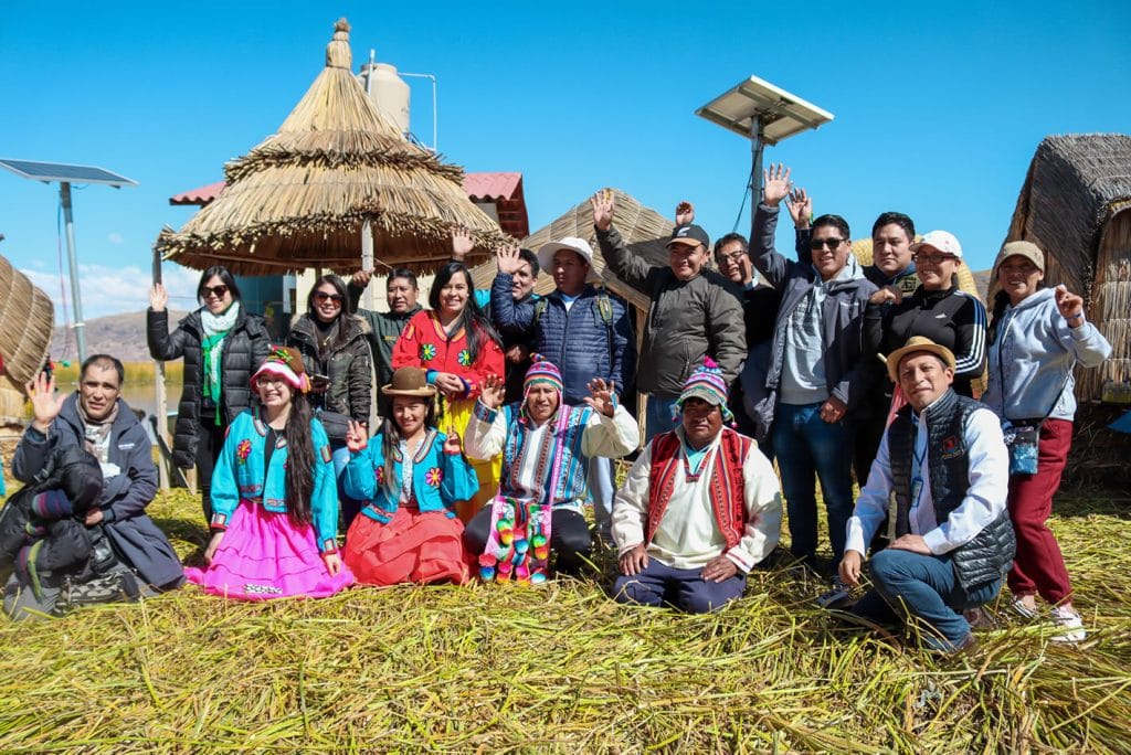 Grupo de turistas posando con lugareños en isla de Uros; tres viajeras usan vestimenta tradicional como muestra de inmersión cultural.