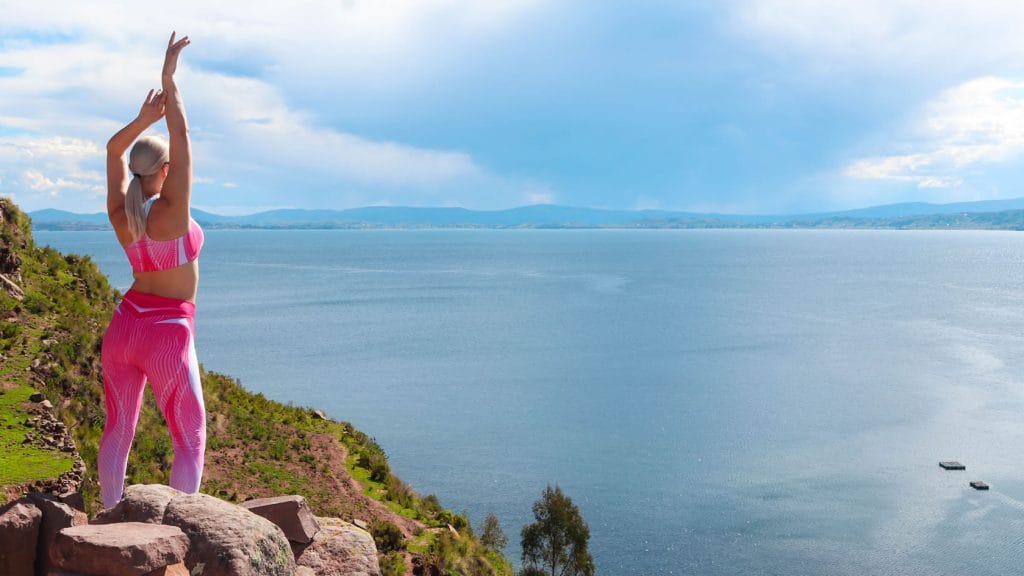 Turista en ropa deportiva haciendo estiramientos en la cima de la Isla Taquile, disfrutando de vistas panorámicas del Lago Titicaca.