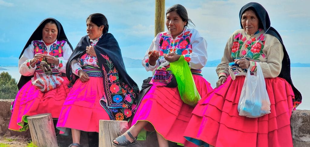 Cuatro mujeres de Amantaní tejiendo artesanías a mano, de fondo una impresionante vista del Lago Mayor Titicaca.