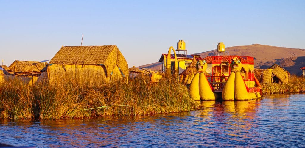 Casas flotantes de totora de los Uros, con balsa catamarán que exhibe doble proa con forma de cabeza de puma, en el Lago Titicaca.