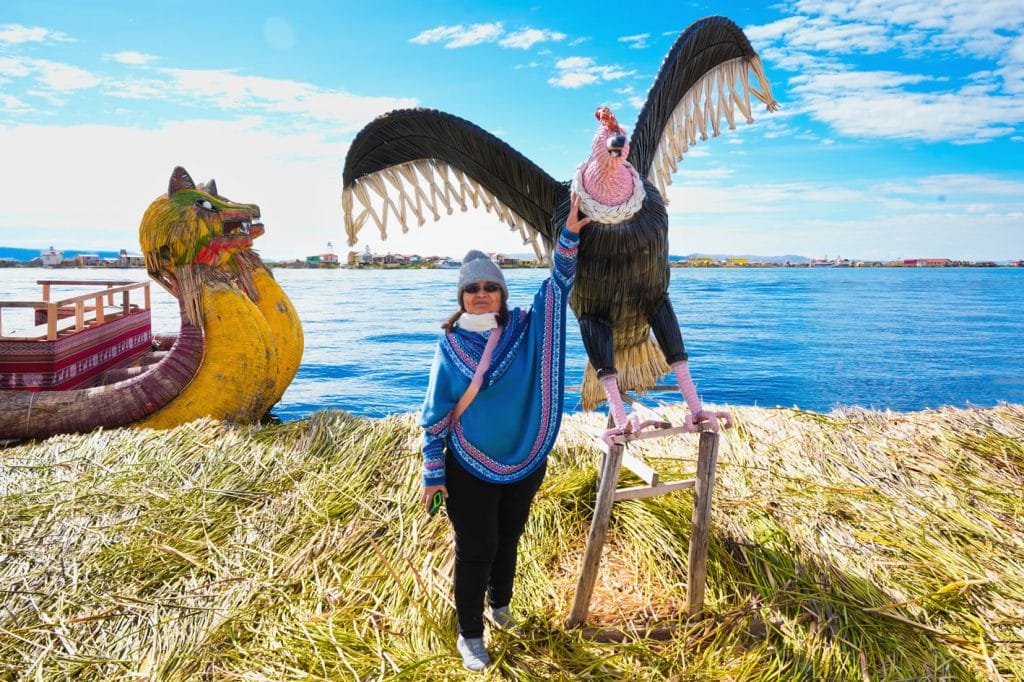 Turista posando con la imponente figura de cóndor andino, una artesanía gigante hecha de totora en las islas de Uros.