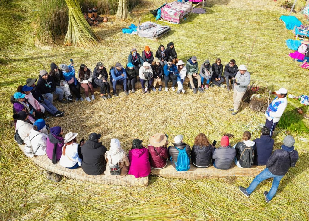 Vista aérea en isla de Uros: Turistas sentados y guía de pie, en la foto destaca claramente el piso de totora flotante.