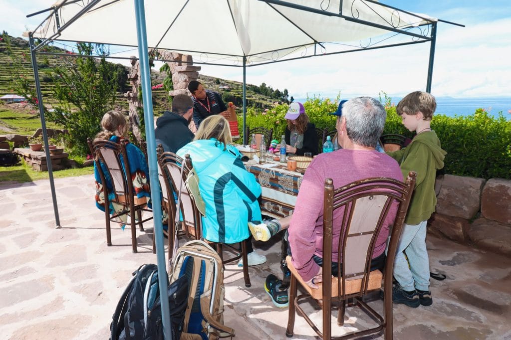 Grupo de turistas almorzando al aire libre en un restaurante familiar de la Isla Taquile, con vistas al Lago Titicaca.