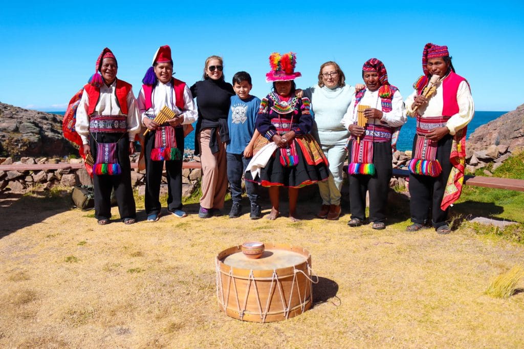 Turistas posando con danzantes de Sikuris de Taquile durante el encuentro cultural dentro de la casa de familia en la isla.