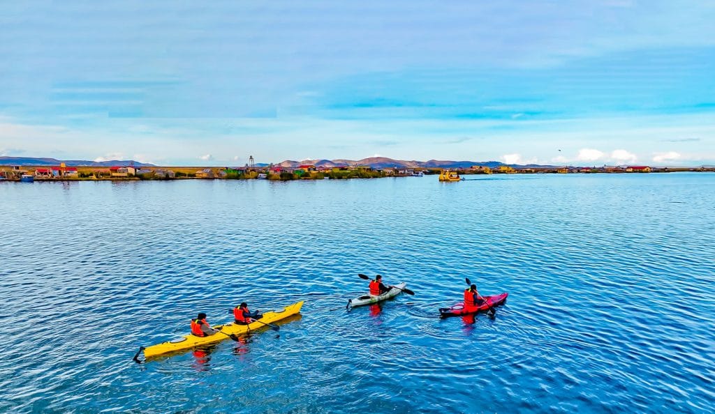 Kayaks navegando en las tranquilas aguas del Lago Titicaca, al fondo las islas flotantes de totora de los Uros.