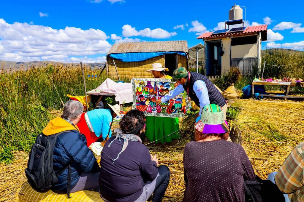 Demostración de arte textil: Mujer Uros y guía explican tejidos a turistas en una isla flotante de totora, Lago Titicaca.