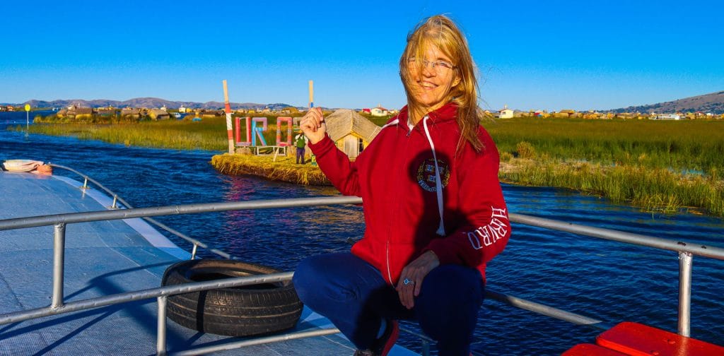 Turista en lancha turística navegando hacia las Islas Flotantes de los Uros. Casas de totora visibles en la distancia, Titicaca.
