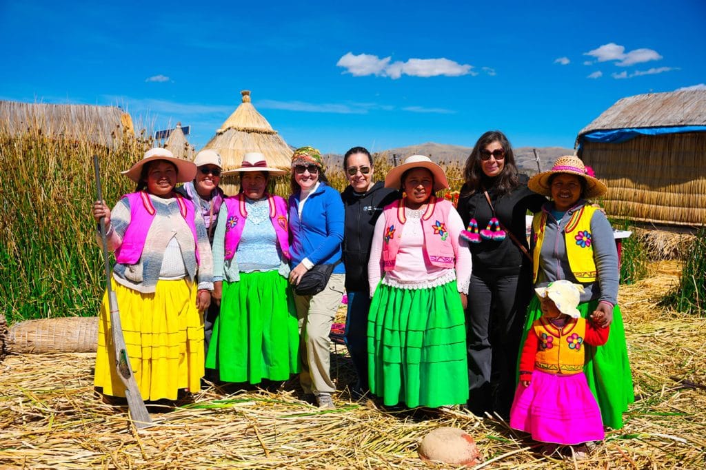 Islas Flotantes de los Uros, Interacción cultural: Mujeres de la comunidad Uros en traje tradicional junto a turistas en una isla de totora, Titicaca.