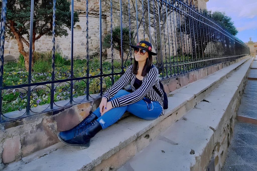 Turista posando en la gradería de la Plaza de Armas con la Iglesia Santiago Apóstol de Lampa detrás.