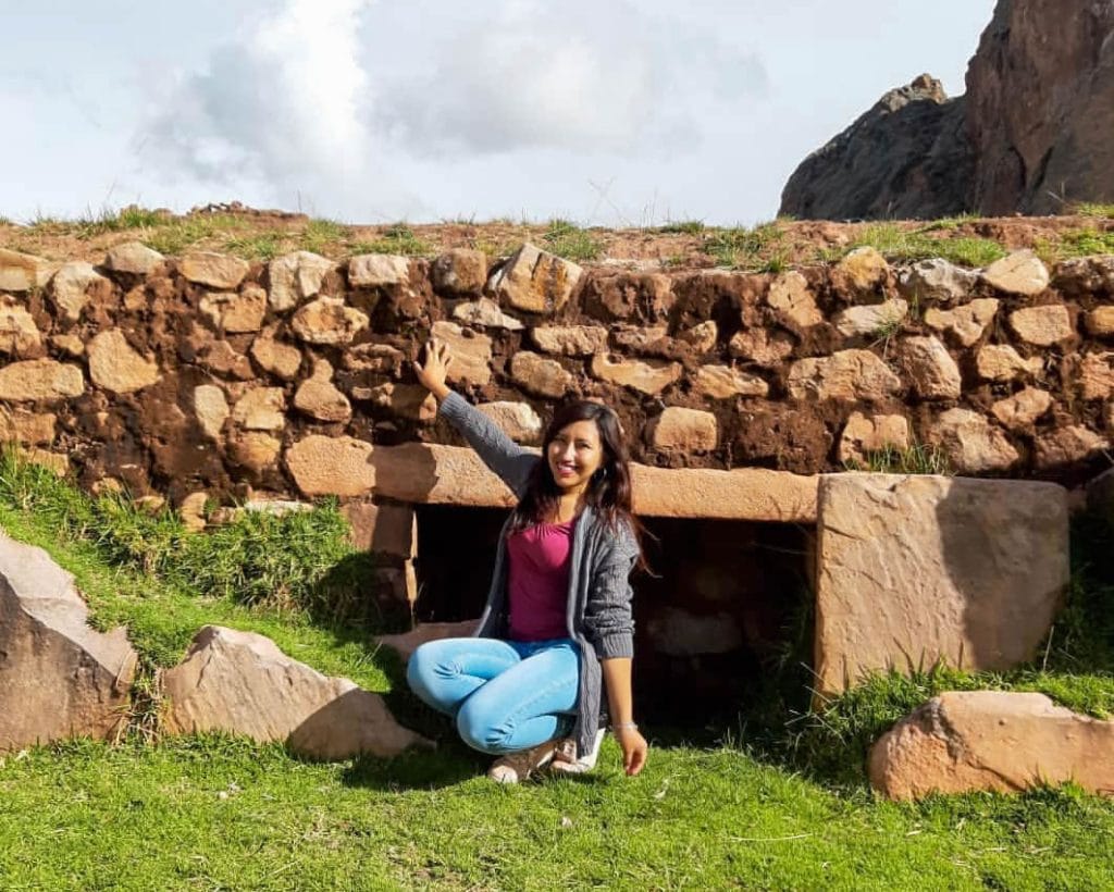 Mujer sonriente en la puerta de una tumba ancestral de piedra de la cultura Pucará.