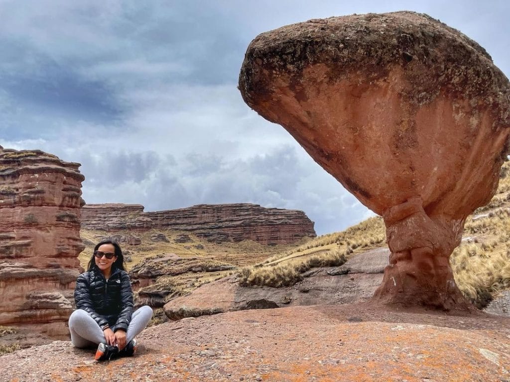 Formación rocosa natural en Tinajani, más ancha arriba y angosta en la base, con viajera sentada en el suelo.