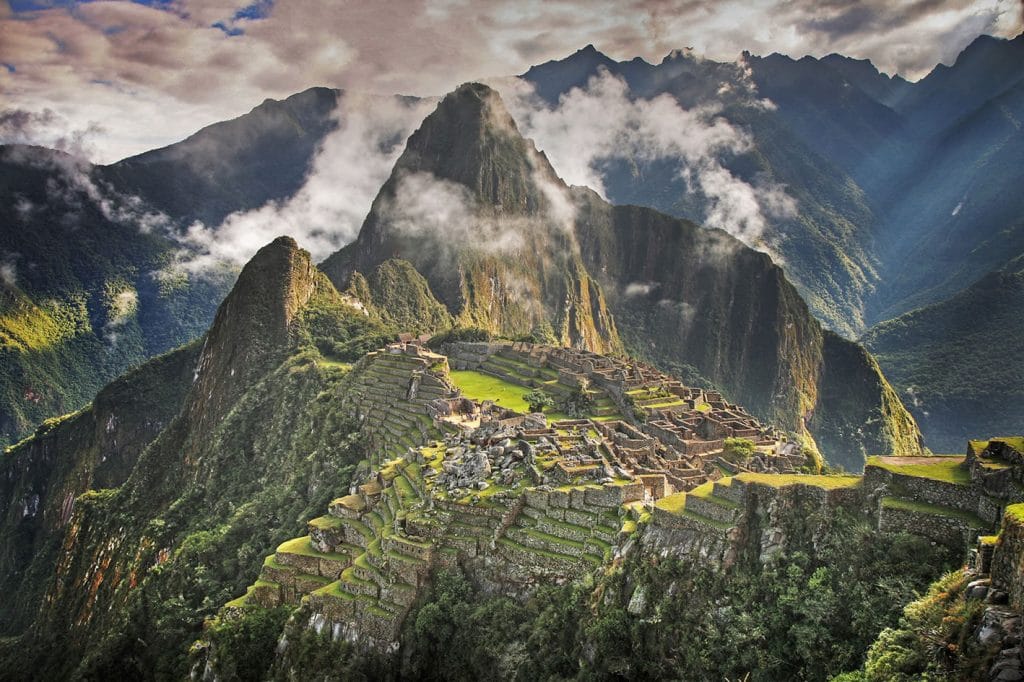 Vista icónica panorámica de la ciudadela inca de Machu Picchu y el Huayna Picchu al fondo, envuelta en neblina.