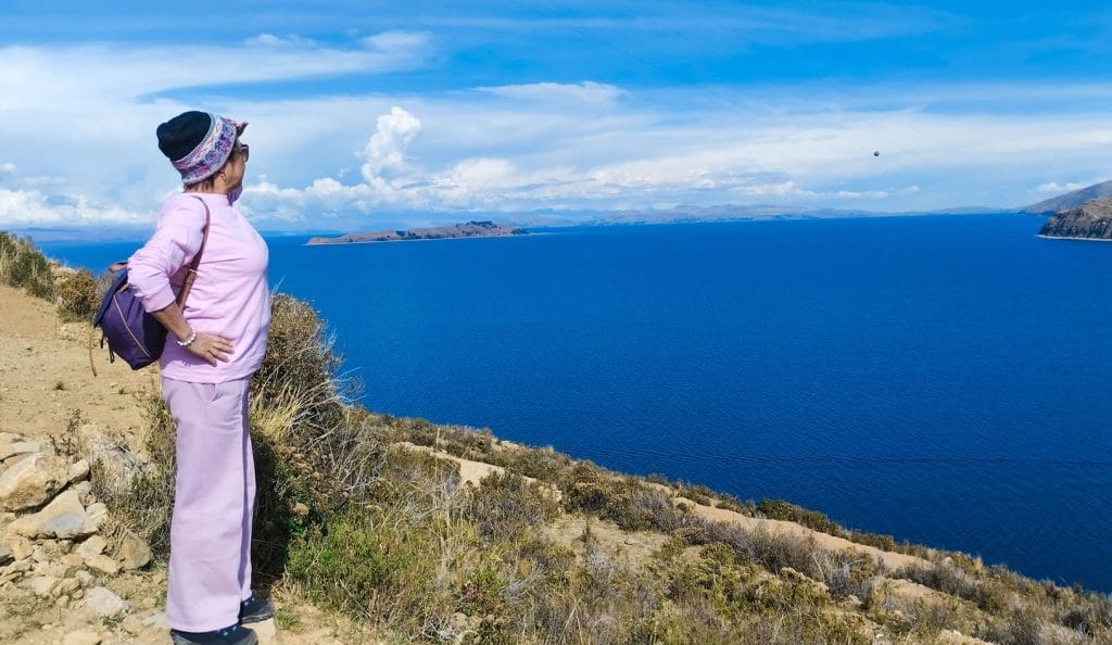 Mujer viajera observando la inmensidad del Lago Titicaca desde un mirador en la parte alta de la Isla del Sol, destacando el vasto horizonte azul del altiplano boliviano.
