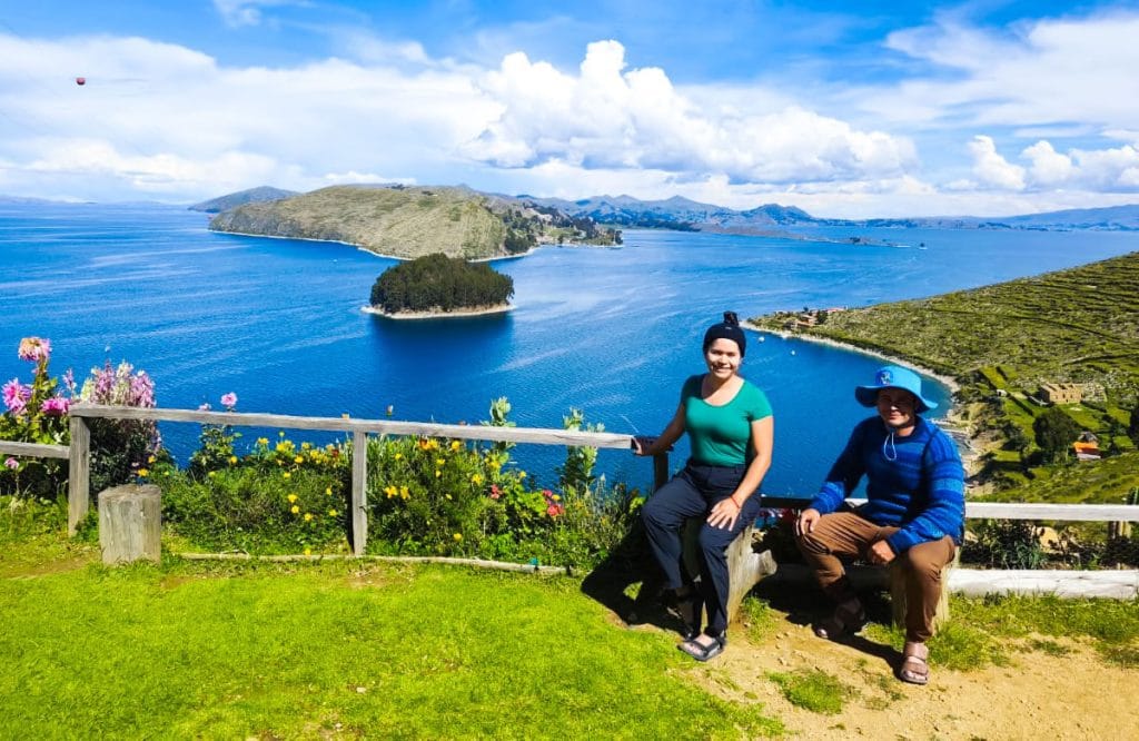Pareja de turistas sentados sobre la parte superior de una casa tradicional en la Isla del Sol, disfrutando de la vista panorámica del vasto Lago Titicaca en el lado boliviano.
