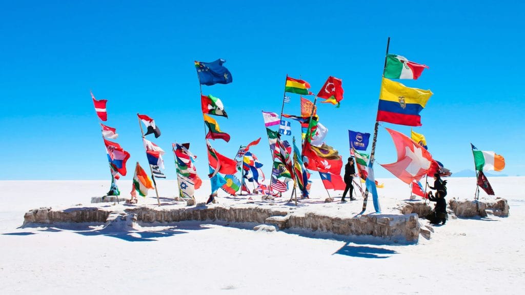 Vista del famoso Parque de Banderas (o Plaza de las Banderas) en la inmensidad blanca del Salar de Uyuni, un punto de encuentro para viajeros y exploradores, destacando el horizonte infinito de sal.