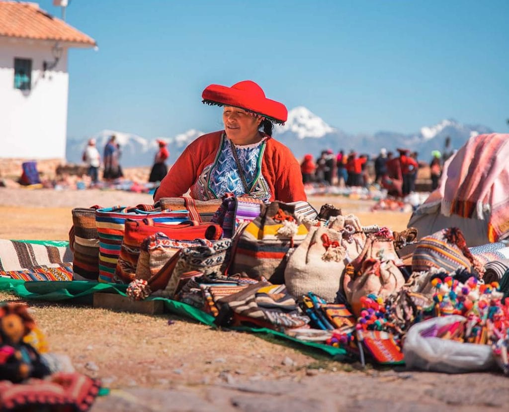 Mujer local vendiendo coloridos textiles andinos y artesanías tradicionales en la plaza principal de Chinchero, Cusco.
