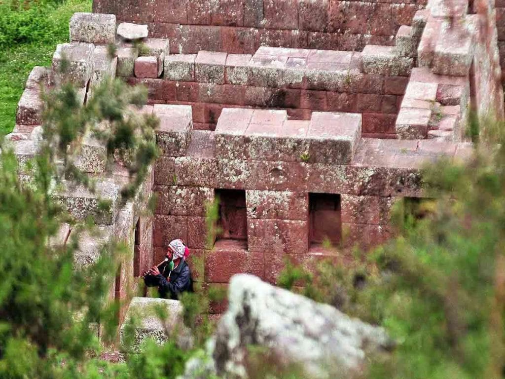 Muros de piedra inca y música tradicional en el Valle Sagrado: Un nativo toca un instrumento andino cerca de las construcciones ancestrales.