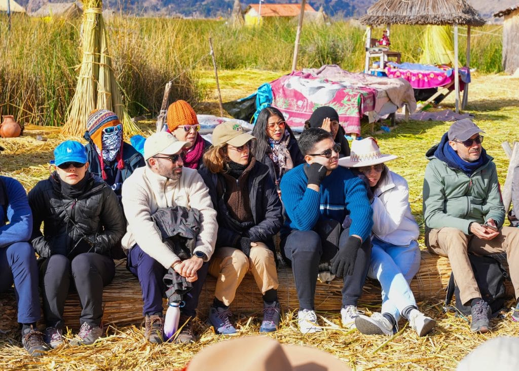 Turistas relajados prestando atención a la exposición cultural del guía de Puno Tours en las islas flotantes de los Uros.