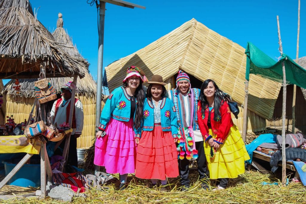 Guía de Puno Tours y tres turistas alegres posando con la vestimenta tradicional de las islas flotantes de los Uros.