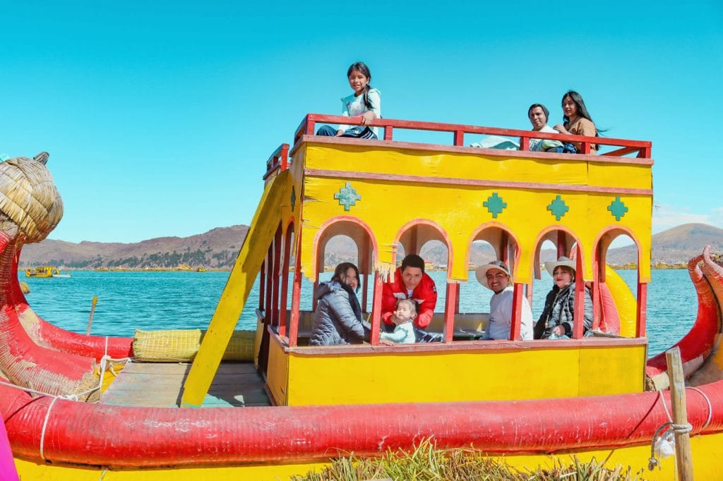 Vista lateral de la balsa catamarán de totora de dos pisos, con turistas navegando en ambos niveles cerca de las islas de los Uros en el Titicaca.