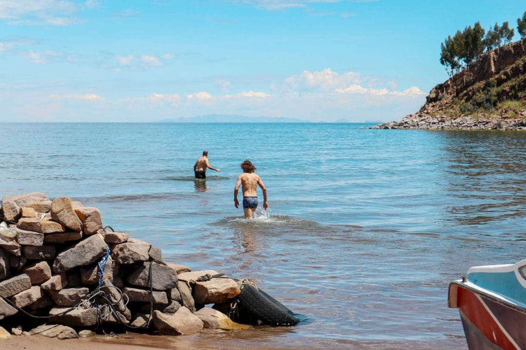 Turistas aventureros disfrutando del contacto con las gélidas aguas del Lago Titicaca en la tranquila bahía de Luquina Chico.