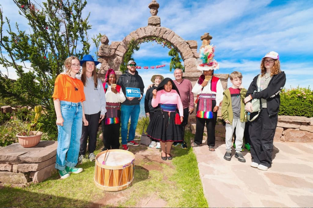 Turistas posando con los dueños de casa en Taquile, recibiendo la bienvenida en la entrada principal con el arco de piedra característico.