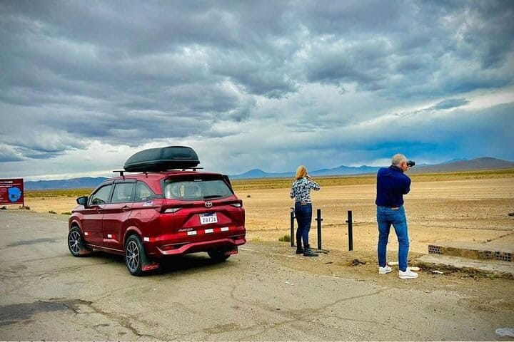 SUV rojo de transporte privado detenido para que la pareja de turistas fotografíe el paisaje del Altiplano, en la ruta Aeropuerto Juliaca - Puno.