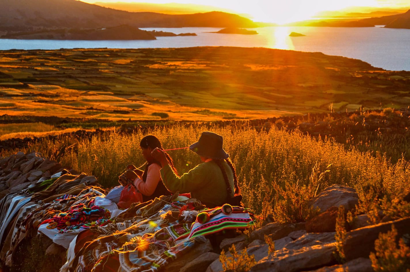 Mujeres en Amantaní tejiendo artesanías con vista al atardecer en el tour Uros y Taquile.