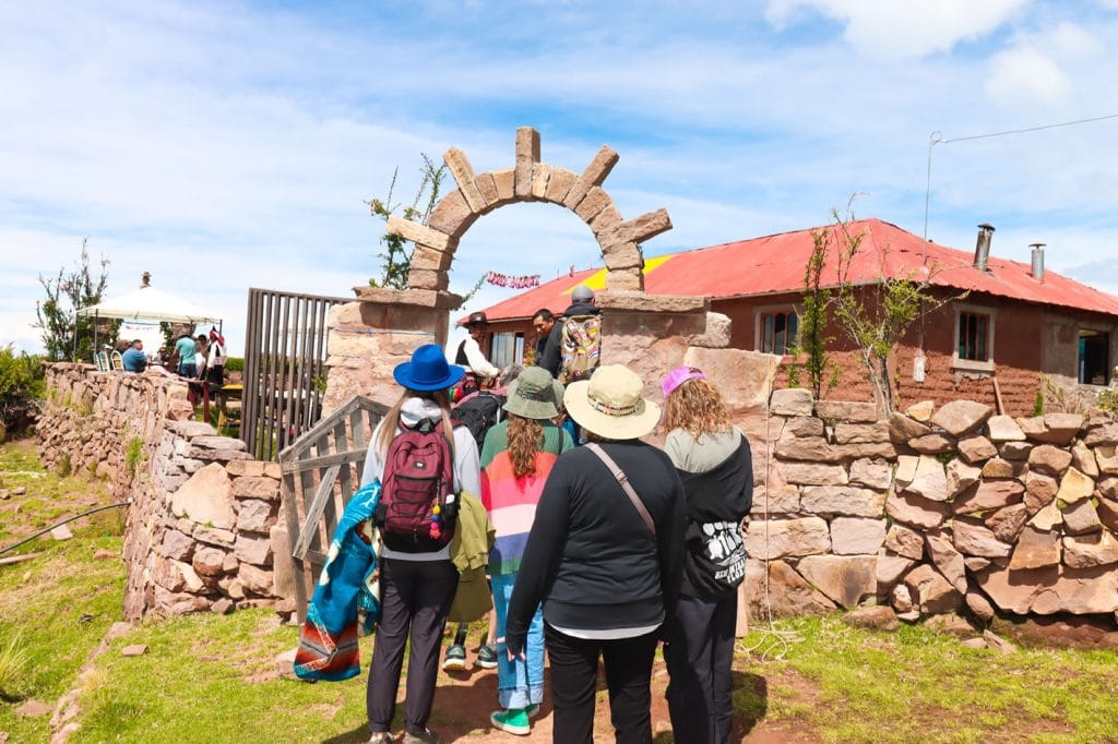 Turistas ingresando al arco de bienvenida de piedra de una casa tradicional en la Isla Taquile, Titicaca.