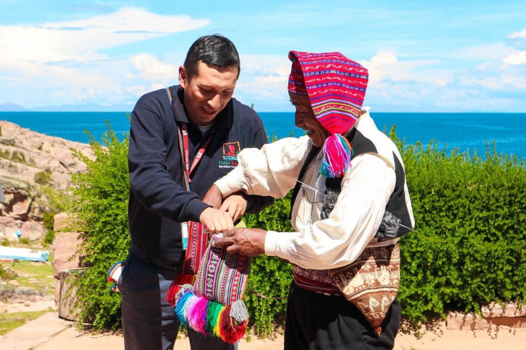 Conexión cultural: Taquileño ofrece hojas de coca a visitante como ritual de bienvenida ancestral en el tour de Uros y Taquile en Puno.