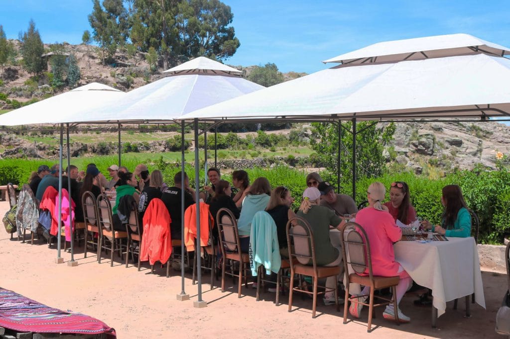 Almuerzo tradicional en Taquile: Grupos de turistas comen bajo toldos en filas, disfrutando de la gastronomía andina con vista al Lago Titicaca.