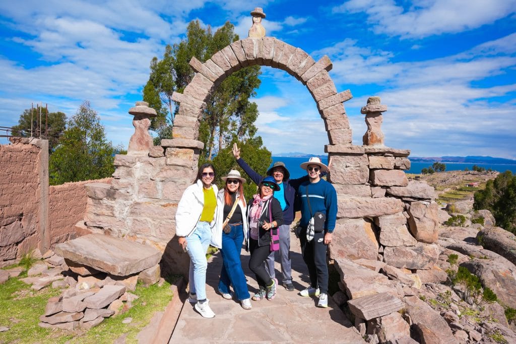 Portal de piedra en Taquile: Cinco turistas alegres posan en el arco de entrada tras subir los más de 550 escalones del puerto, Lago Titicaca.