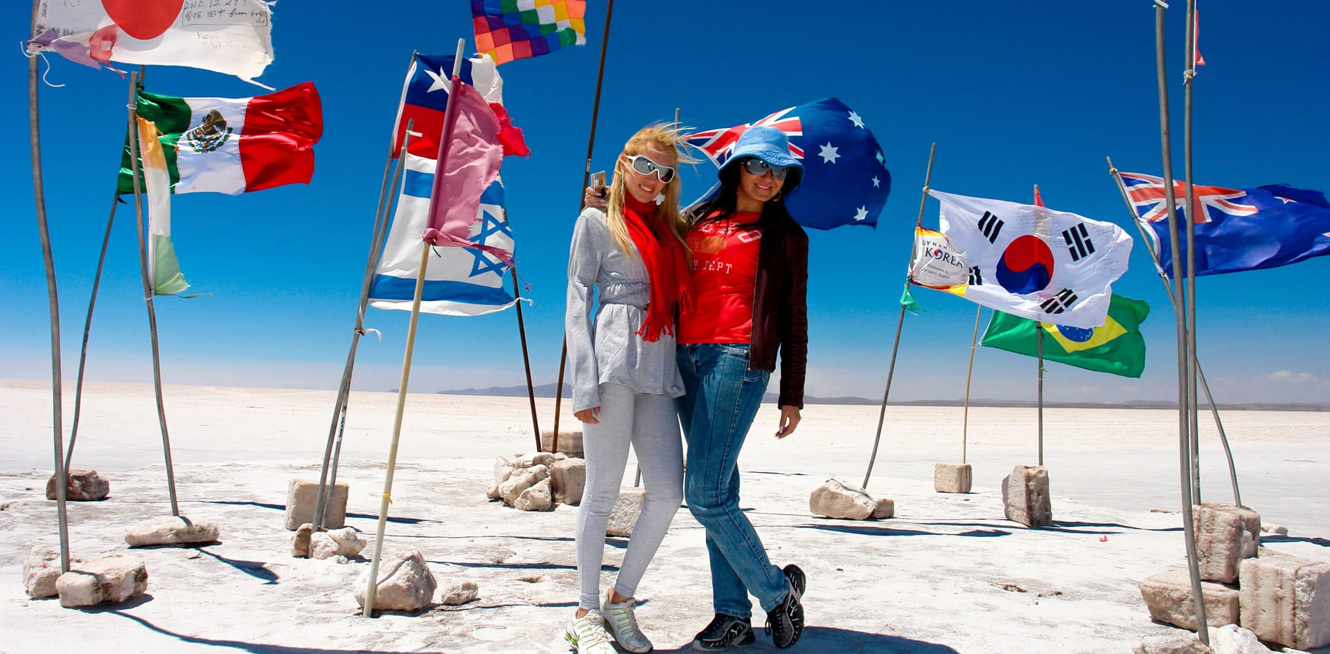 Dos viajeras posando con banderas en el icónico Salar de Uyuni, parte de nuestros tours a Bolivia y Perú.